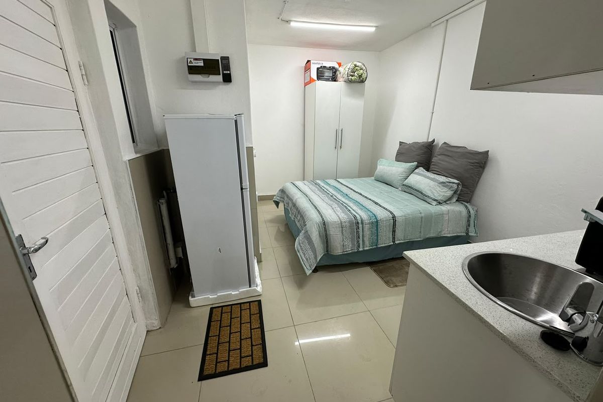 Compact open-plan studio space featuring tiled flooring, a small kitchenette area with a stainless steel sink, and direct access via a louvered door.
