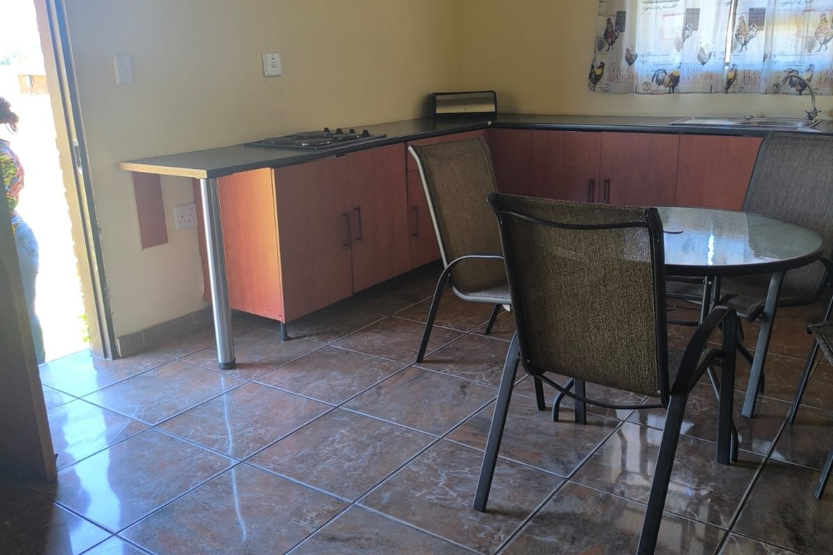 A functional kitchen area featuring built-in cabinetry, laminate countertops, a built-in hob, and tiled flooring under a traditional thatched roof structure.