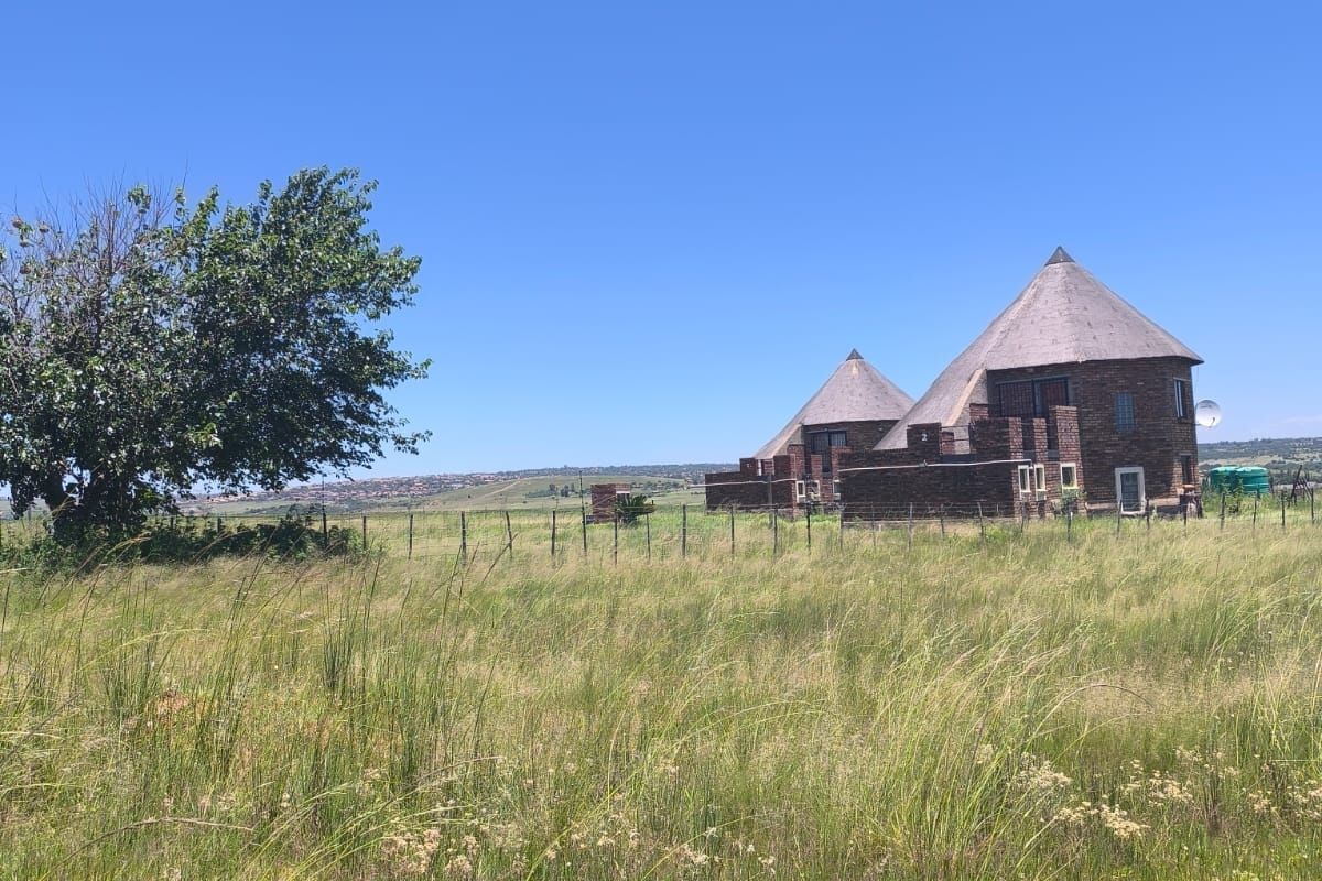 A view of the rear elevation of a face brick farmhouse with distinctive thatched roofs, set within a large open field.