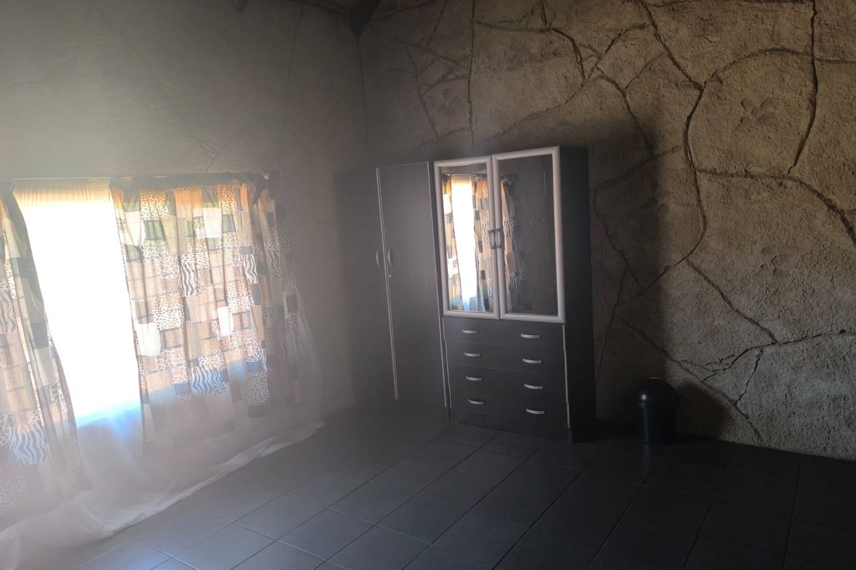 A bedroom featuring unique textured stone-effect walls, dark tiled flooring, and a high thatched ceiling, offering a rustic farm-style aesthetic.
