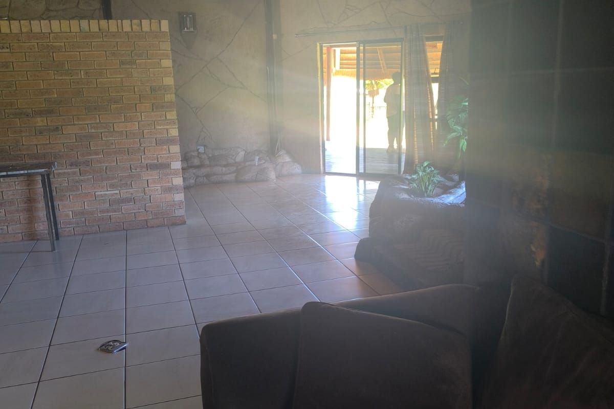 Spacious living area featuring a high thatched roof with exposed rafters, ceramic tiled flooring, and sliding doors leading to an outdoor patio.