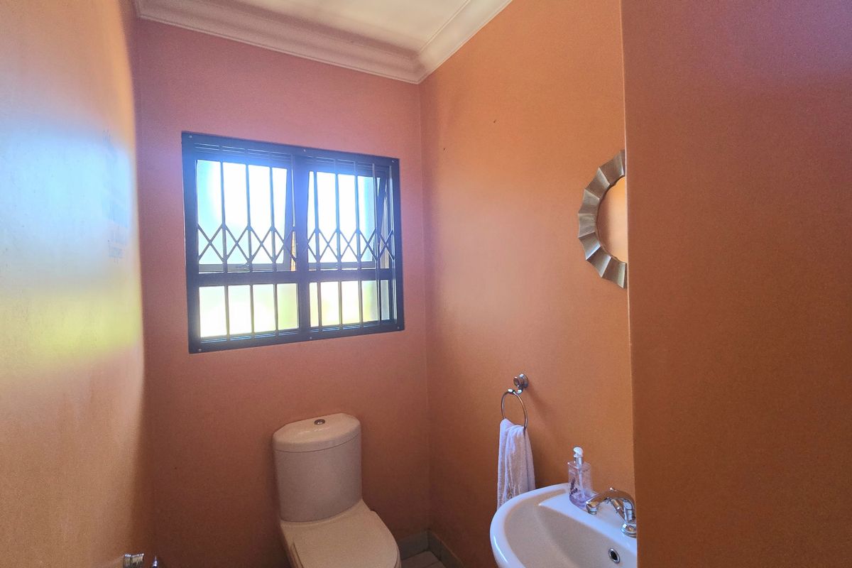 A compact guest bathroom featuring a pedestal basin, toilet, and security bars on the window, finished with vibrant orange wall paint.