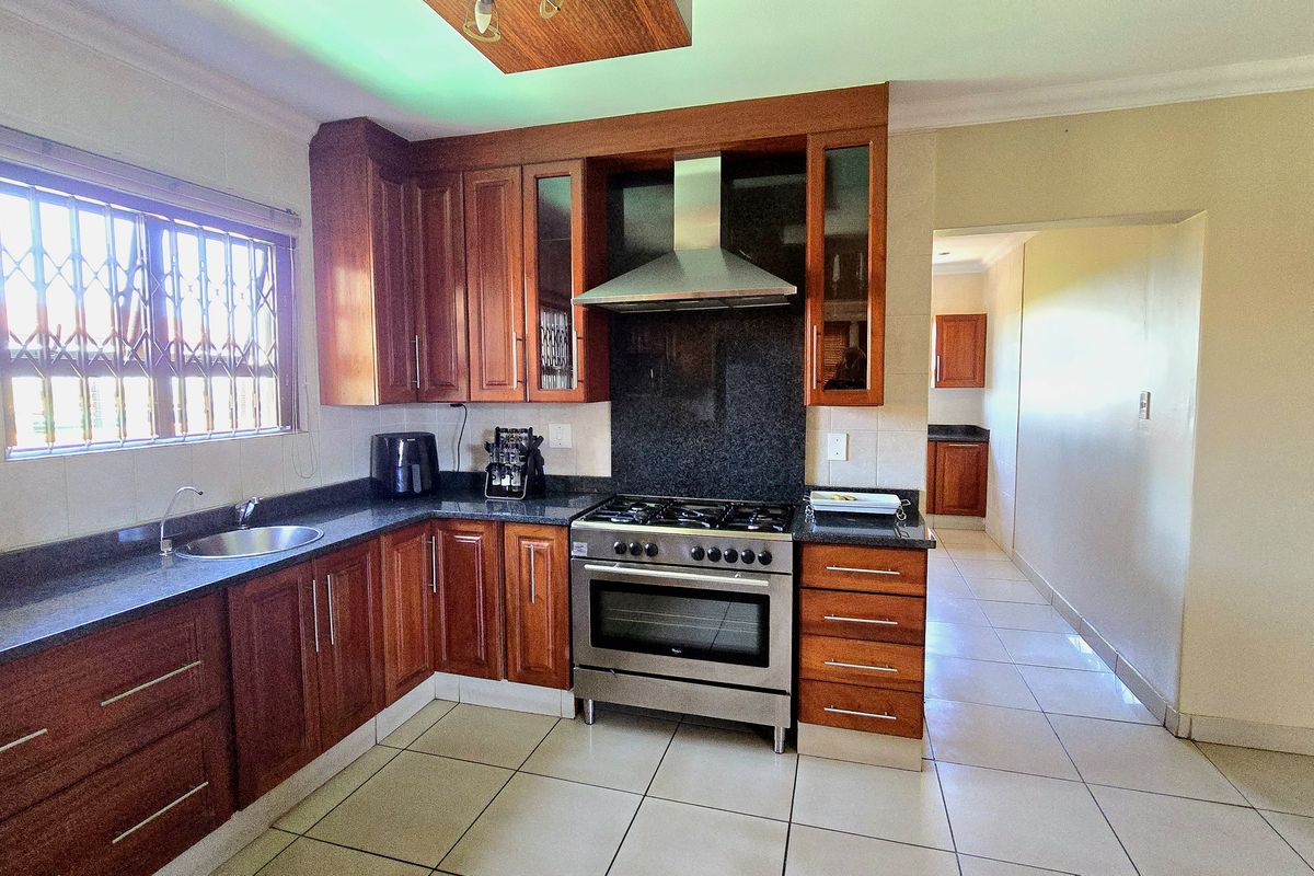 A functional kitchen featuring warm wooden cabinetry, granite countertops, a stainless steel gas stove with extractor fan, and tiled flooring.