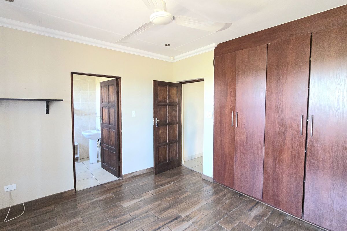 A spacious bedroom featuring wood-look tiled flooring, extensive built-in cupboards, a ceiling fan, and direct access to an en-suite bathroom.