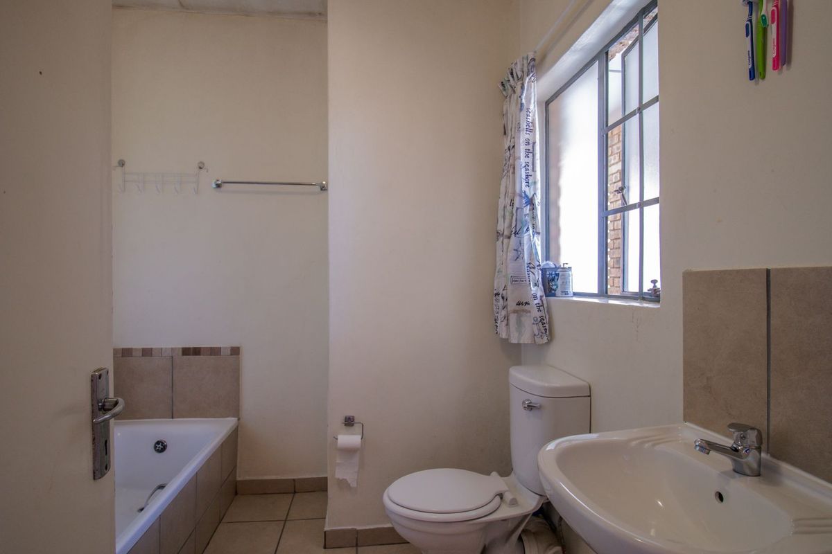 A functional bathroom featuring a built-in bathtub, pedestal washbasin, and toilet with neutral tiled flooring and splashbacks.
