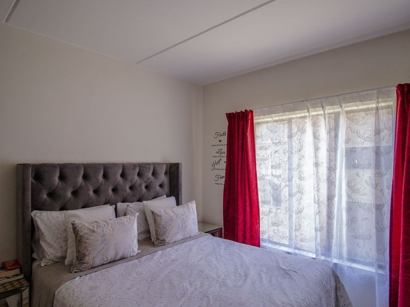 A well-lit bedroom featuring neutral walls and a large window with decorative curtains, providing a comfortable and functional living space.