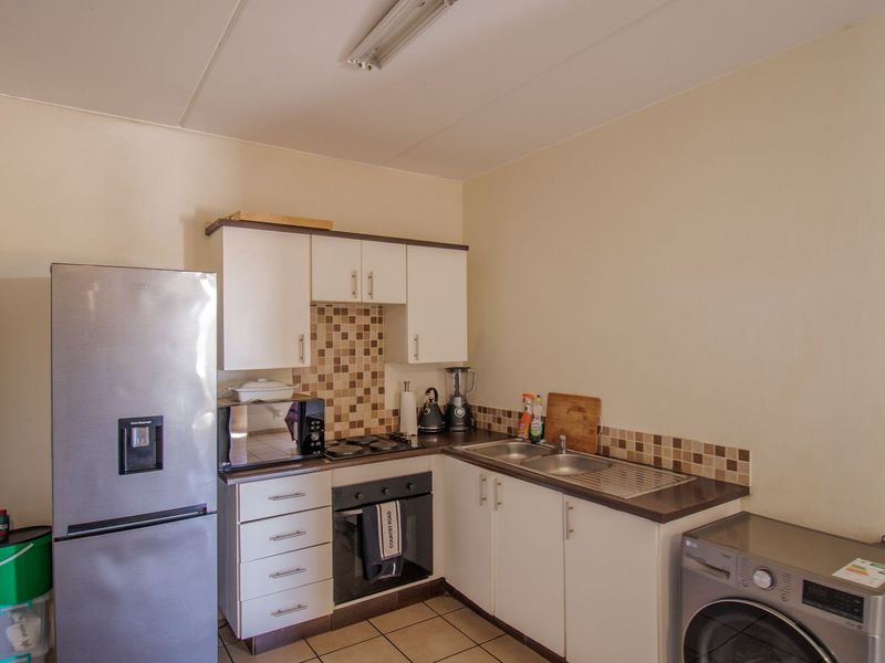 Compact kitchen featuring white cabinetry, mosaic tile backsplash, built-in oven, electric hob, and double bowl sink with ceramic tiled flooring.