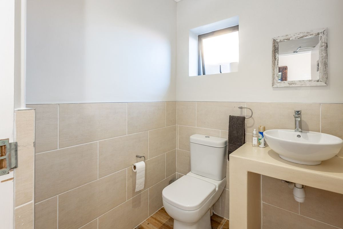 A compact, modern bathroom featuring a vessel sink on a tiled vanity, a white toilet, and neutral wall tiling.