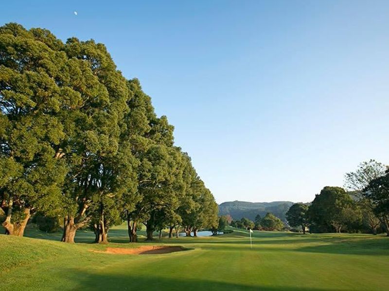 A scenic view of a well-maintained golf course fairway lined with mature trees and a sand bunker.