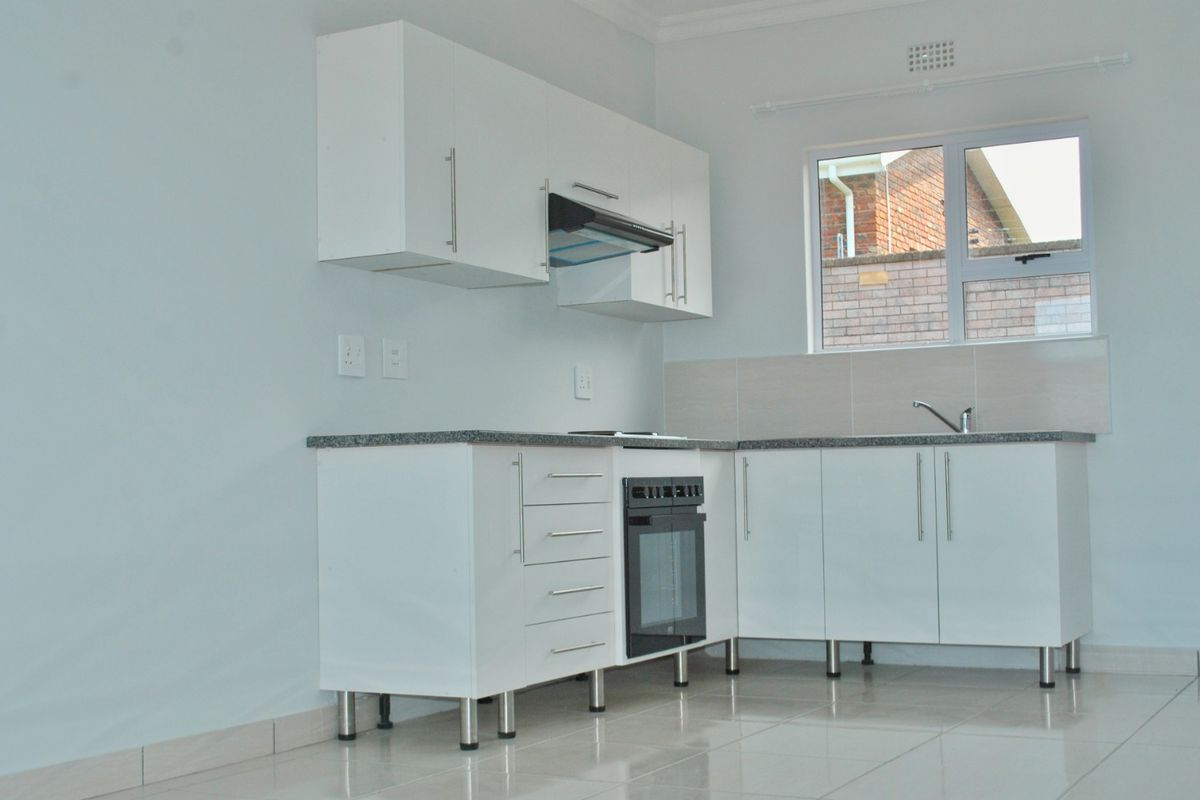 A clean, modern kitchen featuring white cabinetry, granite countertops, built-in oven, extractor fan, and tiled flooring in a bright, open space.