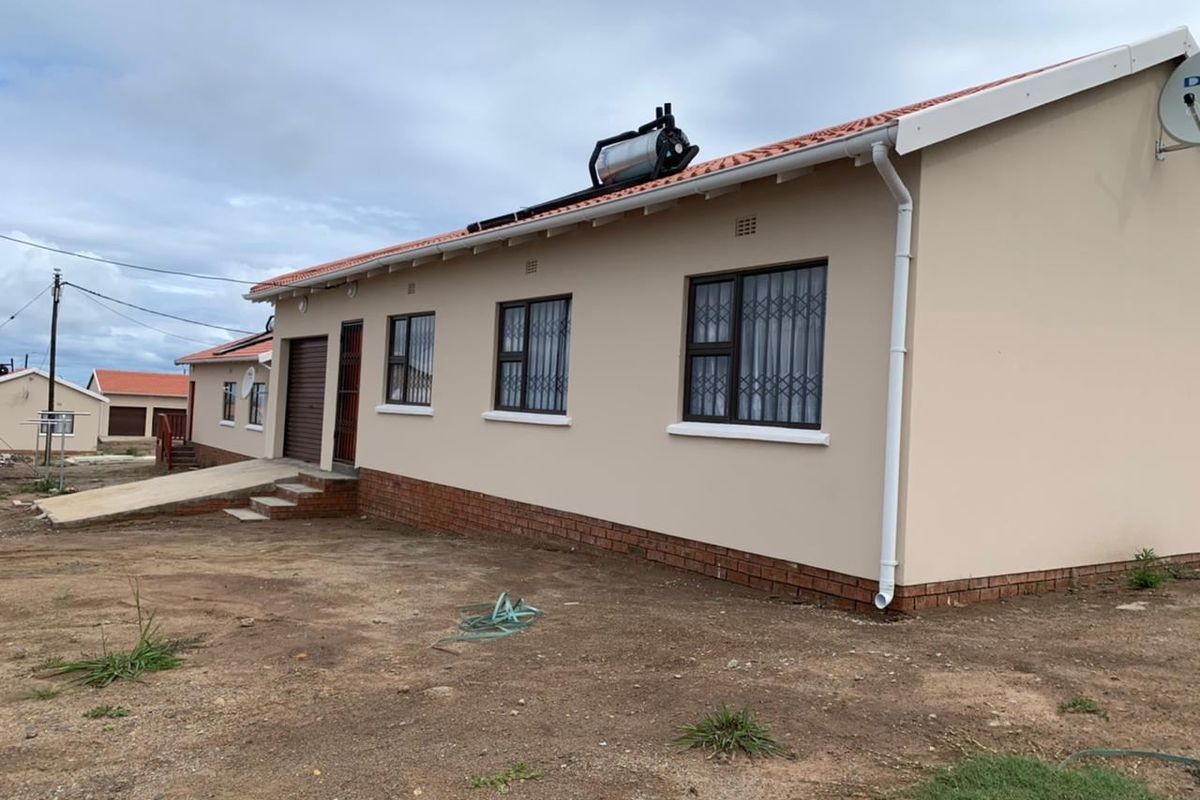 Rear view of a single-story house featuring a solar water heater, brick plinth foundation, and security bars on the windows.