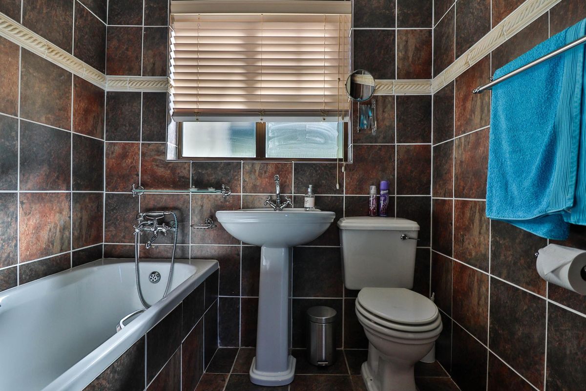 A compact bathroom featuring a pedestal basin, toilet, and a bathtub with a shower mixer, finished with dark, textured wall tiles.