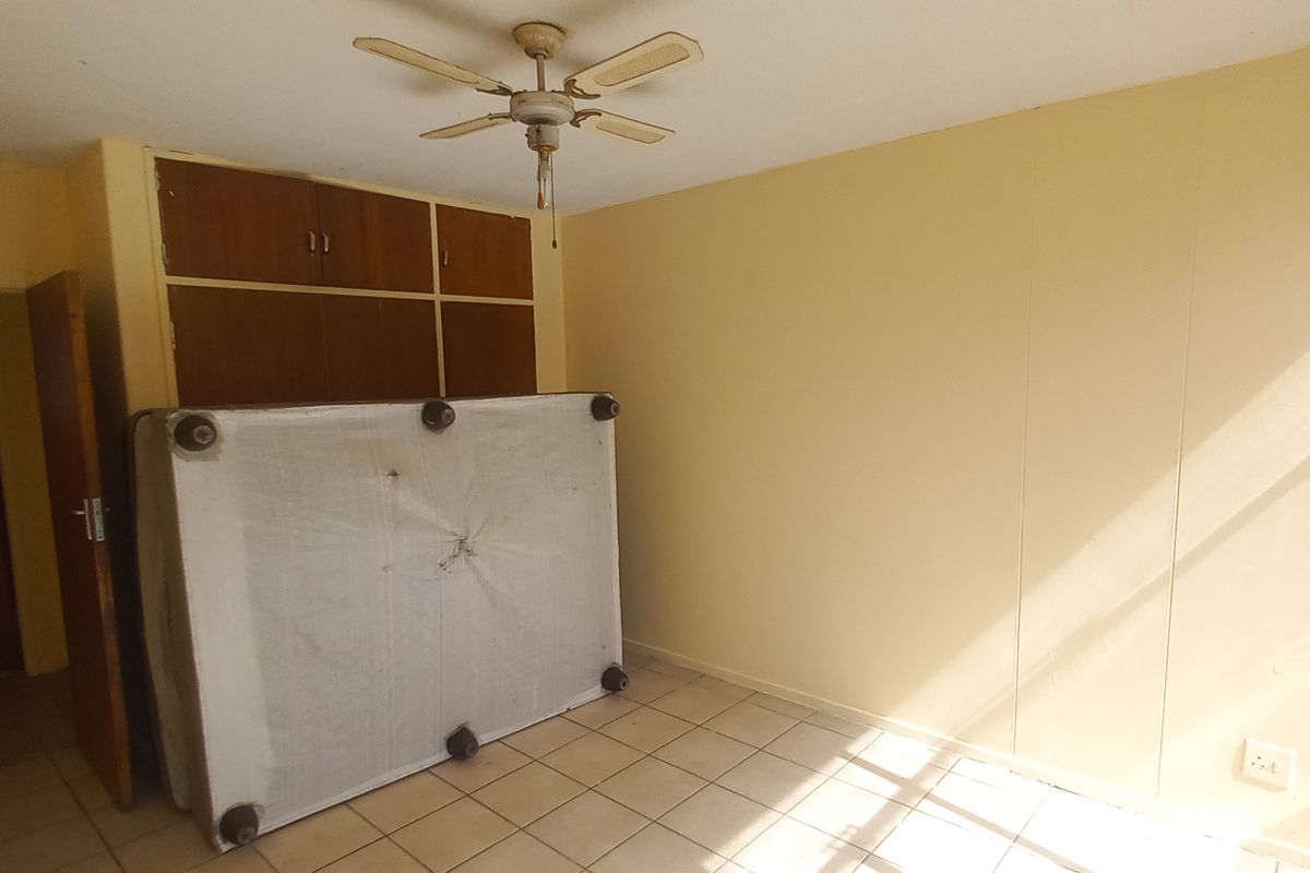 A bedroom featuring tiled flooring, built-in wooden cupboards, and a ceiling fan, offering a blank canvas for renovation or restyling.