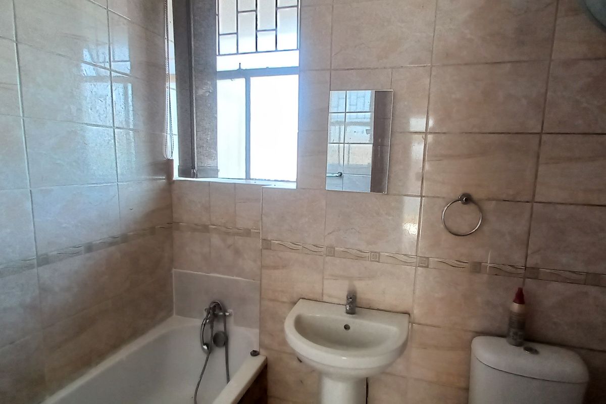 A functional bathroom featuring a bathtub, pedestal basin, and toilet, finished with neutral wall and floor tiles.
