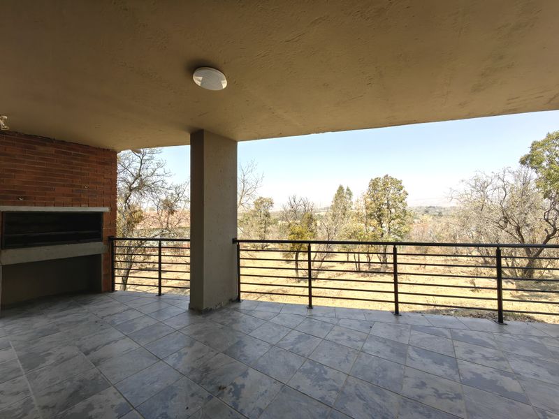 Covered balcony featuring a built-in braai, tiled flooring, and metal balustrade, offering an open view of the surrounding landscape.