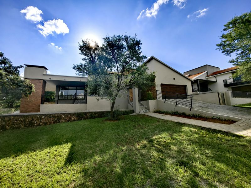 Front elevation of a modern house featuring a paved driveway, integrated garage, stone retaining wall, and a covered patio area.