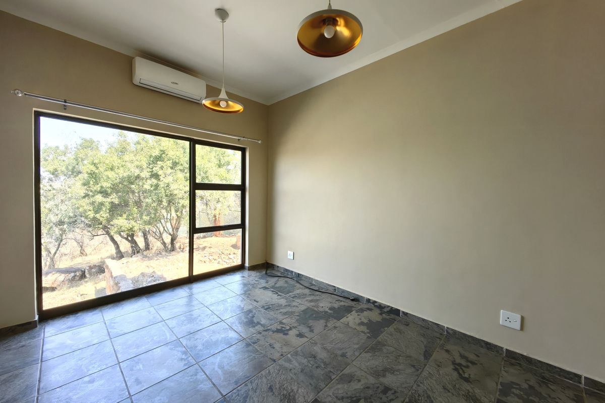 A bright, empty bedroom featuring tiled flooring, a split-system air conditioner, and a large sliding glass door with natural views.