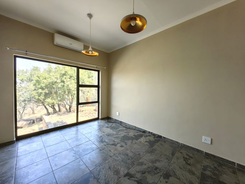 A bright, empty bedroom featuring tiled flooring, a split-system air conditioner, and a large sliding glass door with natural views.