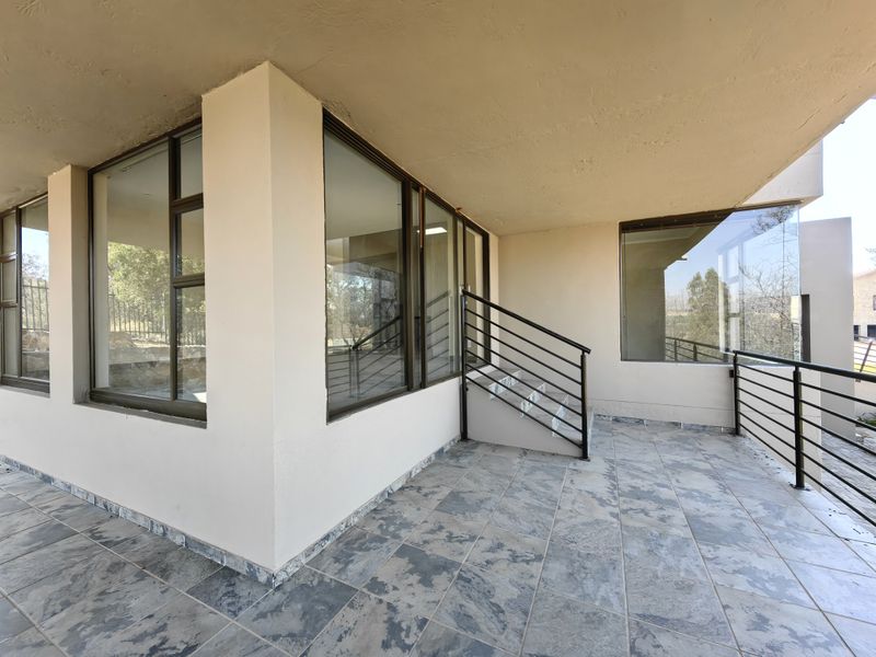 A spacious covered patio featuring tiled flooring, metal balustrades, and large glass windows, offering a clean and modern outdoor living space.