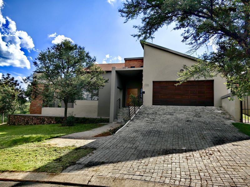 Front elevation of a modern house featuring a paved driveway, double garage, and a combination of rendered walls and stone cladding.