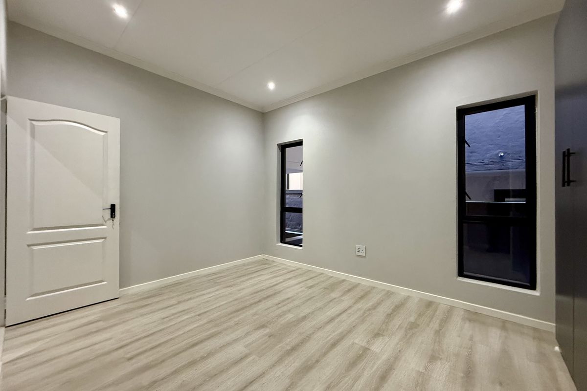 A bright, modern, and empty bedroom featuring neutral walls, laminate flooring, recessed lighting, and built-in wardrobe storage.