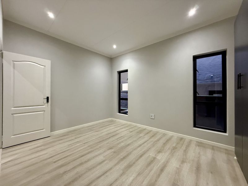 A bright, modern, and empty bedroom featuring neutral walls, laminate flooring, recessed lighting, and built-in wardrobe storage.