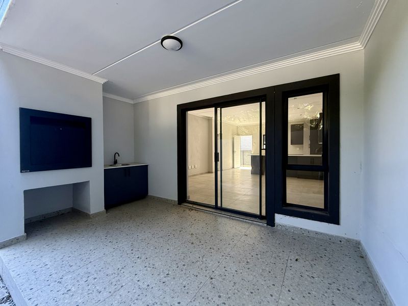 Covered patio featuring a built-in braai, sink, and large sliding glass doors providing seamless access to the interior living space.