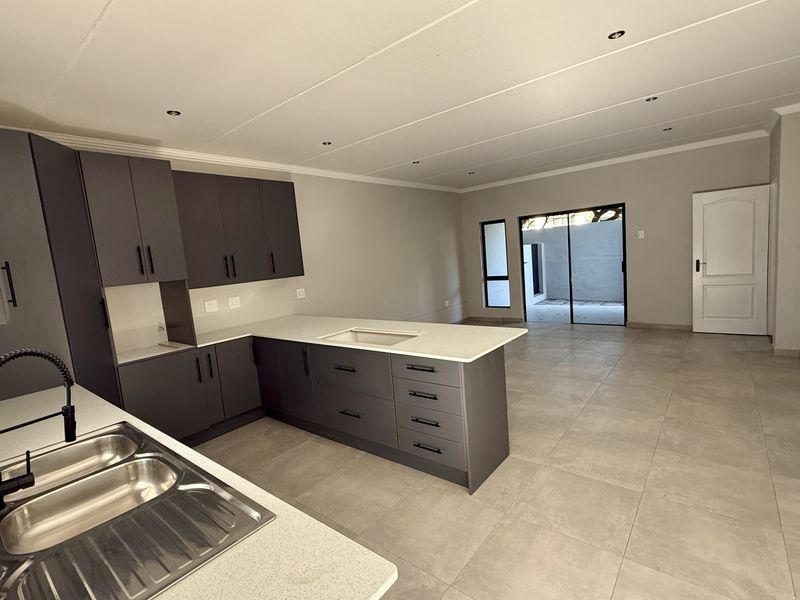 Modern open-plan kitchen and living area featuring sleek dark cabinetry, stone countertops, tiled flooring, and direct access to an outdoor patio space.