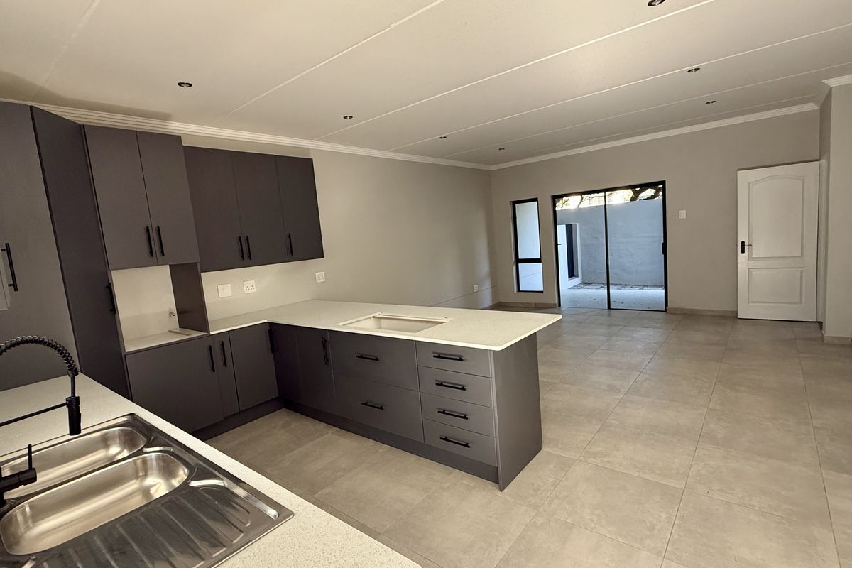 Modern open-plan kitchen and living area featuring sleek dark cabinetry, stone countertops, tiled flooring, and direct access to an outdoor patio space.