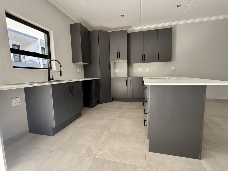 Modern kitchen featuring dark grey cabinetry, white quartz countertops, a central island, and tiled flooring in a clean, contemporary finish.