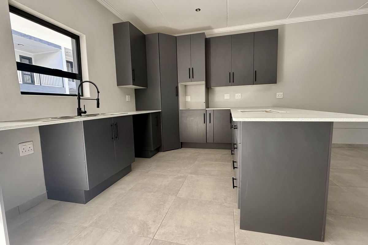 Modern kitchen featuring dark grey cabinetry, white quartz countertops, a central island, and tiled flooring in a clean, contemporary finish.