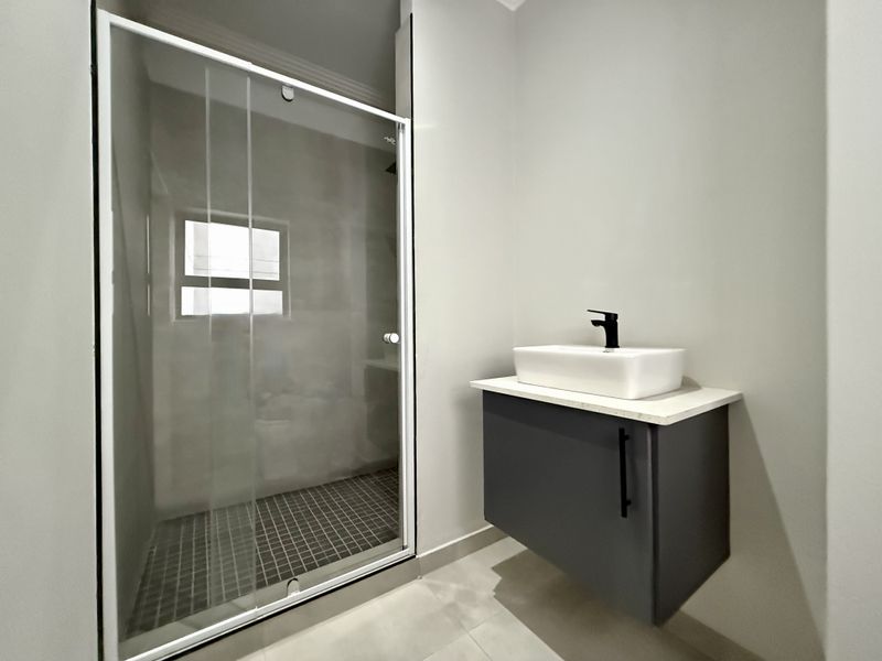 Modern bathroom featuring a floating vanity with a vessel sink, black fixtures, and a glass-enclosed shower with tiled flooring.
