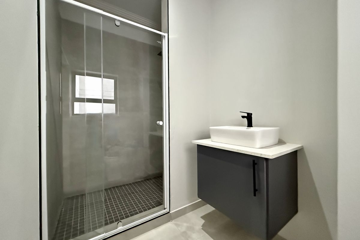 Modern bathroom featuring a floating vanity with a vessel sink, black fixtures, and a glass-enclosed shower with tiled flooring.