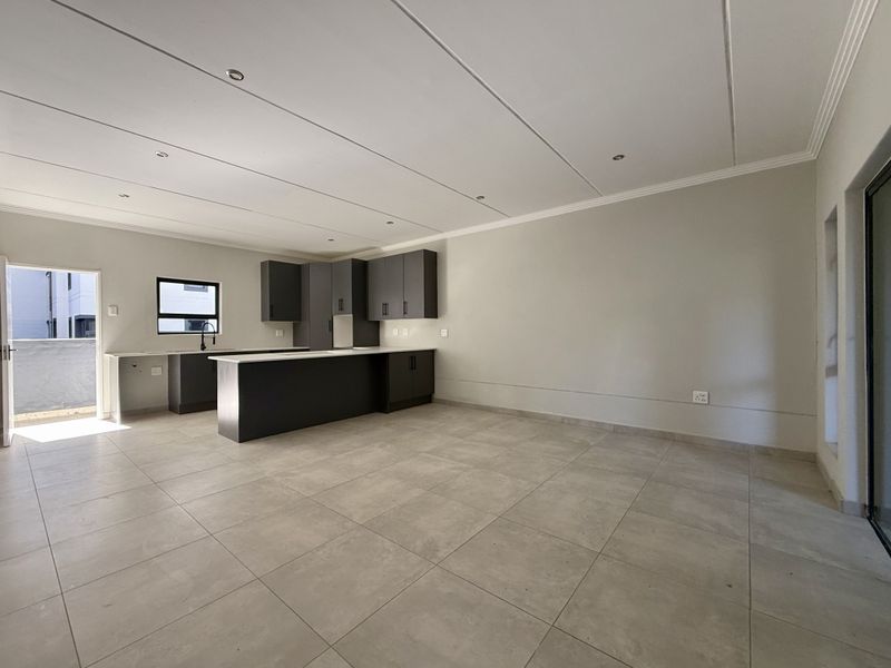 Spacious open-plan living area featuring modern dark cabinetry, a kitchen island, neutral tiled flooring, and recessed lighting, leading to an outdoor patio area.