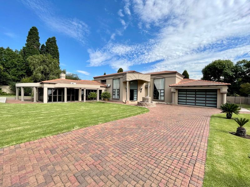 A well-maintained single-story residence featuring a paved driveway, double garage, covered patio area, and a landscaped front garden with a stone fountain.