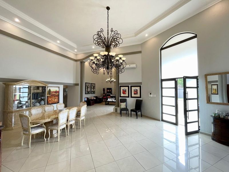 Spacious open-plan living and dining area featuring high ceilings, elegant wrought iron chandeliers, polished tile flooring, and a grand arched entrance.