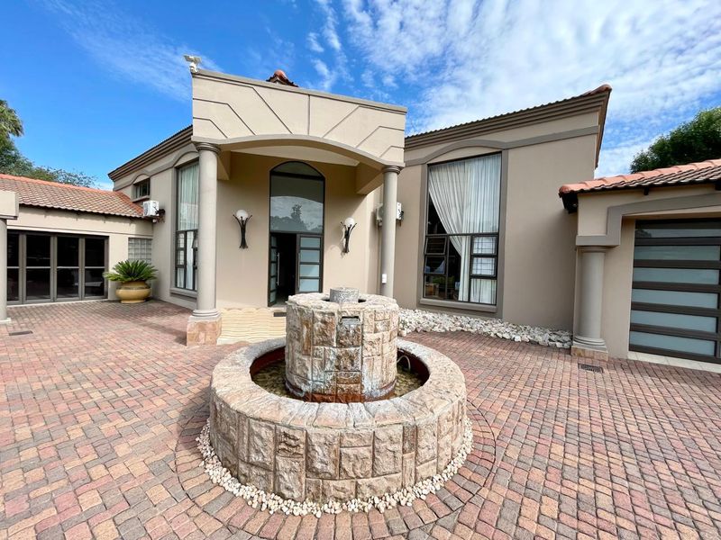 Front exterior view of the house featuring a paved driveway, a prominent stone fountain, and a covered entrance with architectural columns.