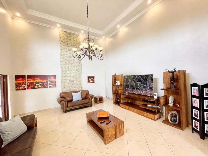 Spacious living room featuring high ceilings with cove molding, recessed lighting, a decorative stone wall accent, and neutral tiled flooring.