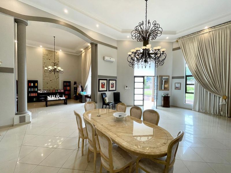 Spacious open-plan living and dining area featuring high ceilings, decorative columns, polished tile flooring, and elegant wrought iron chandeliers.