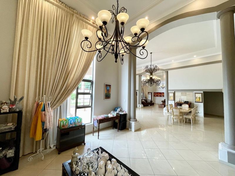 Spacious open-plan living and dining area featuring high ceilings, elegant structural columns, polished floor tiles, and grand decorative chandeliers.