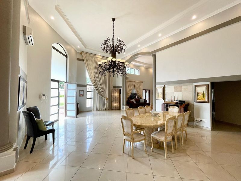 Spacious open-plan living and dining area featuring high ceilings, large arched windows, polished tile flooring, and an elegant wrought iron chandelier.