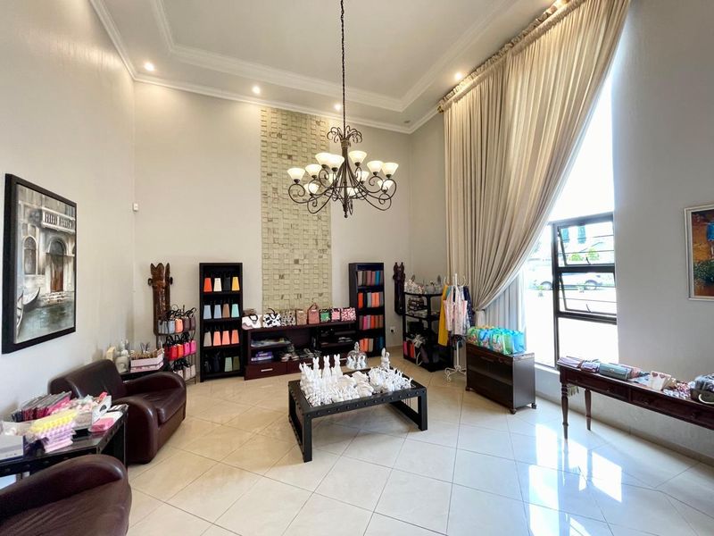 Spacious living area featuring high ceilings, a decorative stone feature wall, elegant chandelier lighting, and large windows with floor-to-ceiling curtains.
