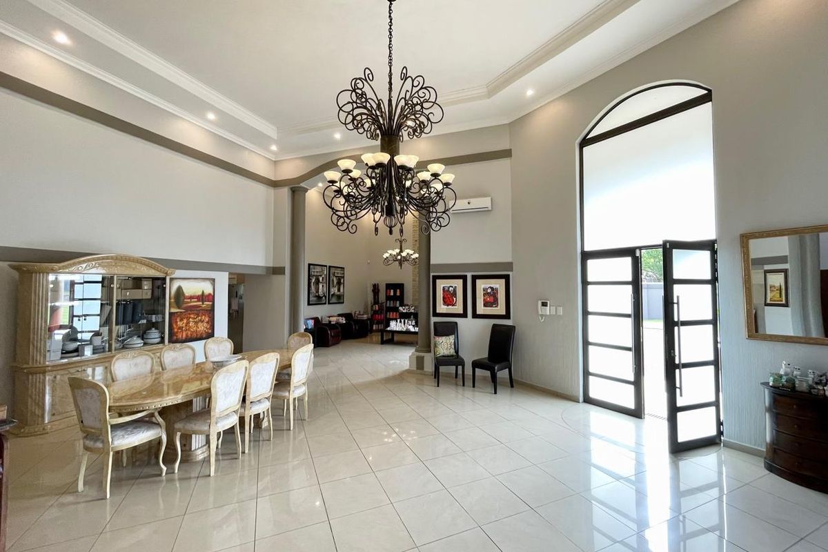 Spacious open-plan living and dining area featuring high ceilings, elegant wrought iron chandeliers, polished tile flooring, and a grand arched entrance.