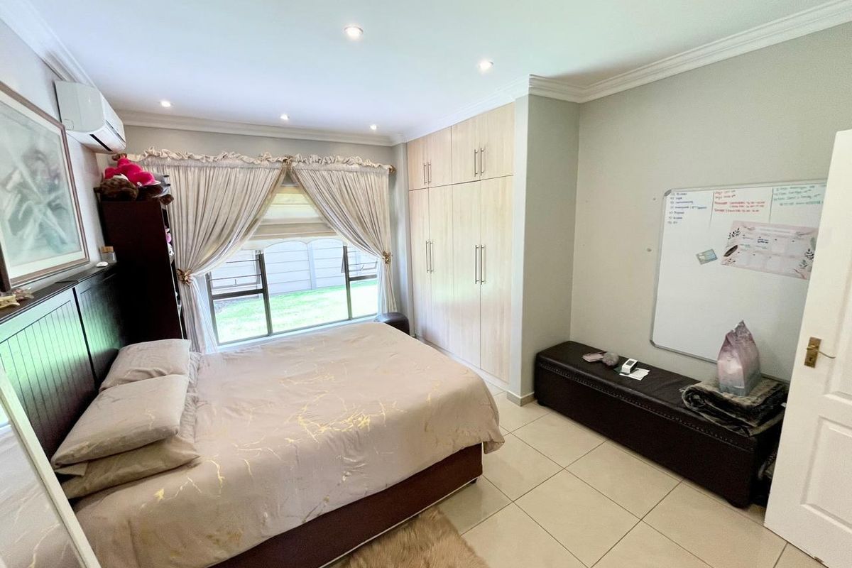 A well-maintained bedroom featuring built-in cupboards, tiled flooring, recessed downlighting, and a wall-mounted air conditioning unit.