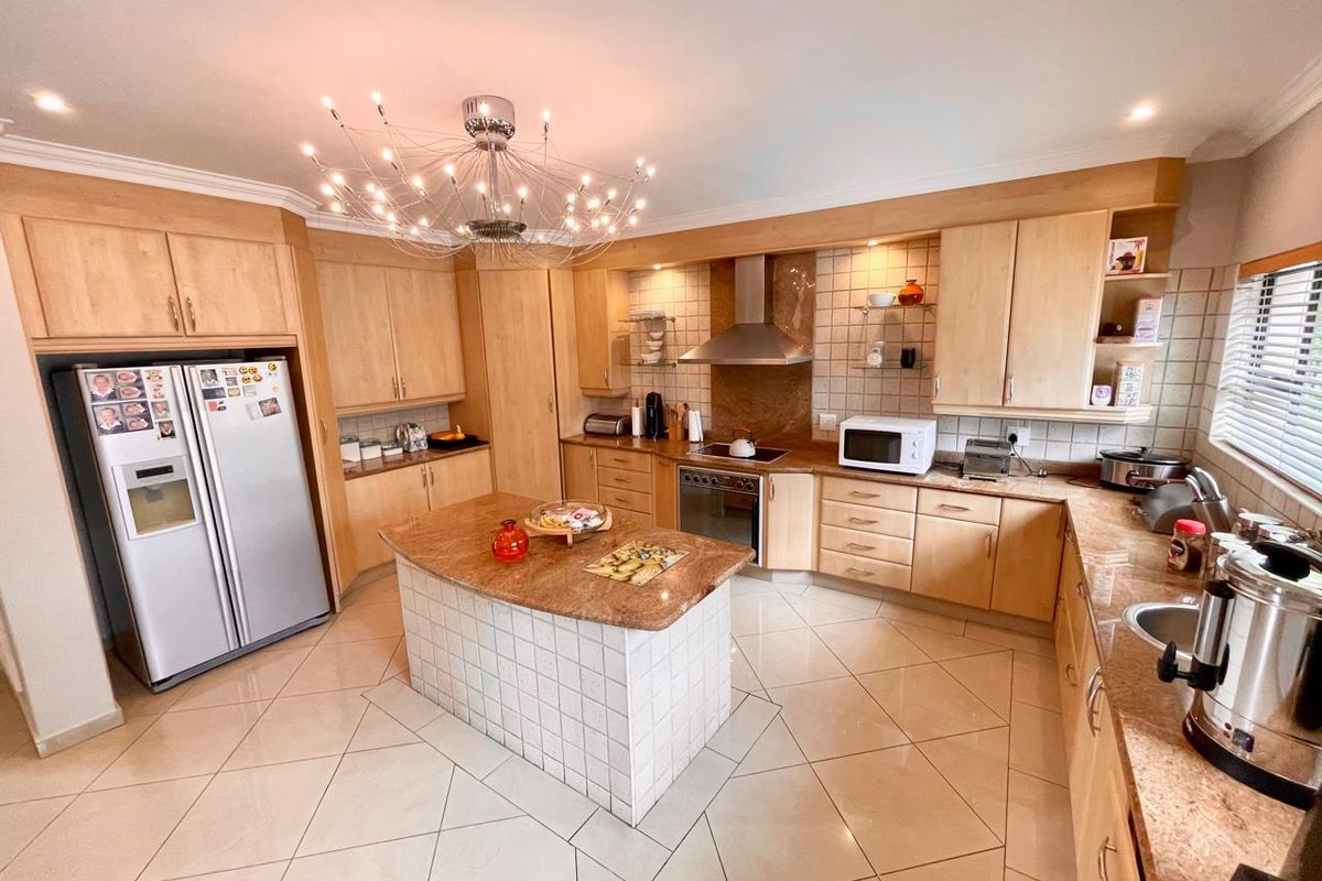 Spacious kitchen featuring light wood cabinetry, granite countertops, a central island, tiled flooring, and modern integrated appliances with a decorative chandelier.