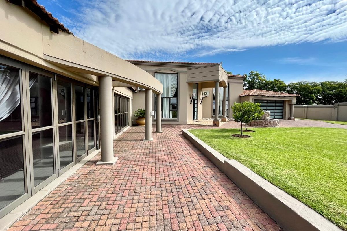 A well-maintained rear exterior featuring a paved patio, covered walkway with columns, expansive lawn, and a modern garage.