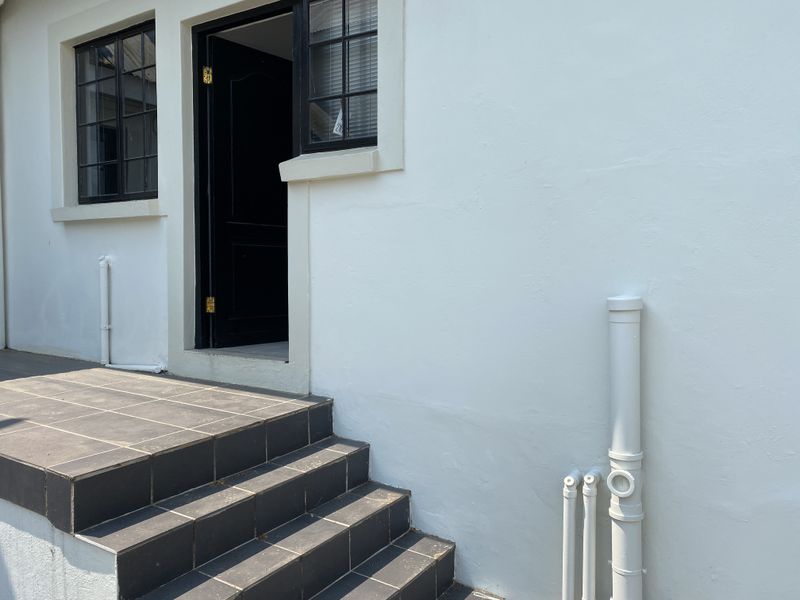 Exterior view of a building entrance featuring tiled steps, black-framed windows, and external plumbing fixtures against a white painted wall.