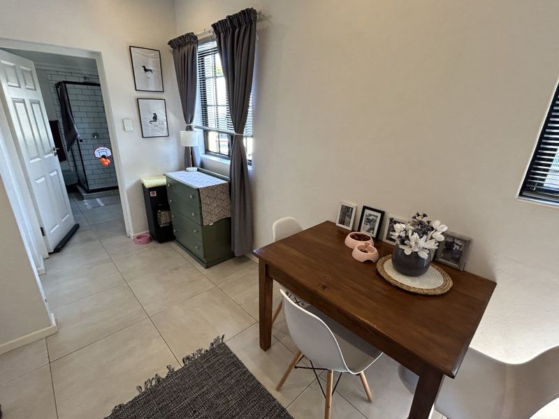A bright dining area featuring neutral tiled flooring, large windows with blinds, and direct access to an adjacent bathroom.