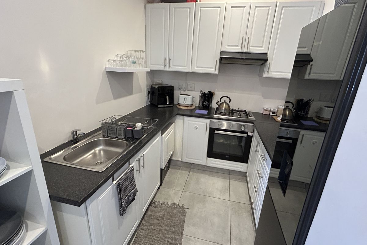 A compact, functional kitchen featuring white cabinetry, dark countertops, built-in oven, gas hob, and tiled flooring.