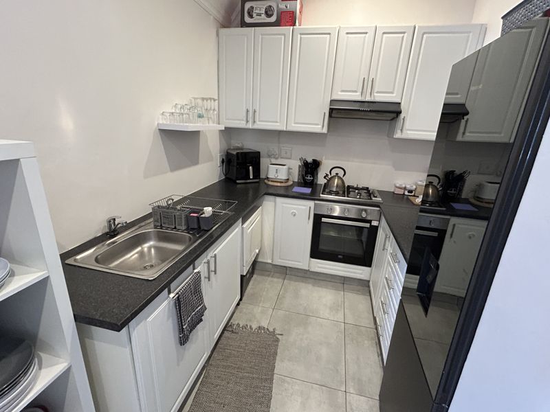 A compact, functional kitchen featuring white cabinetry, dark countertops, built-in oven, gas hob, and tiled flooring.